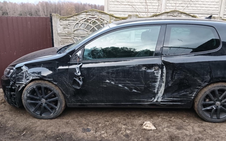 Uszkodzony czarny samochód zaparkowany przy ogrodzeniu.