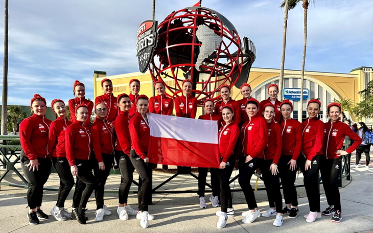Grupa dziewczyn w czerwonych strojach z flagą Polski w rękach.
