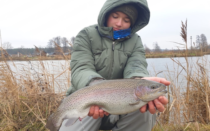 Chłopiec trzyma dużą rybę nad brzegiem wody.