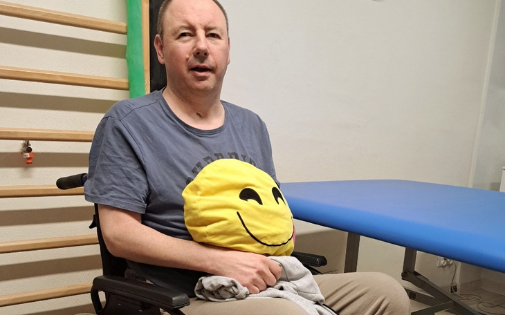 Mężczyzna w wózku inwalidzkim z uśmiechniętą poduszką.