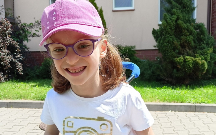 Uśmiechnięta dziewczynka w różowej czapce, bawiąca się na świeżym powietrzu.