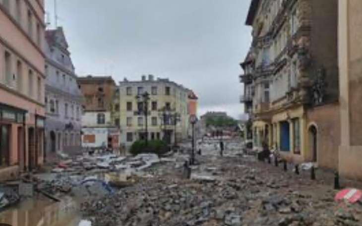 Zniszczona ulica po powodzi, z gruzem i uszkodzonymi budynkami.