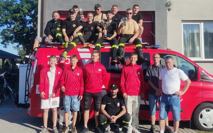 Grupa strażaków pozująca przy wozie strażackim.