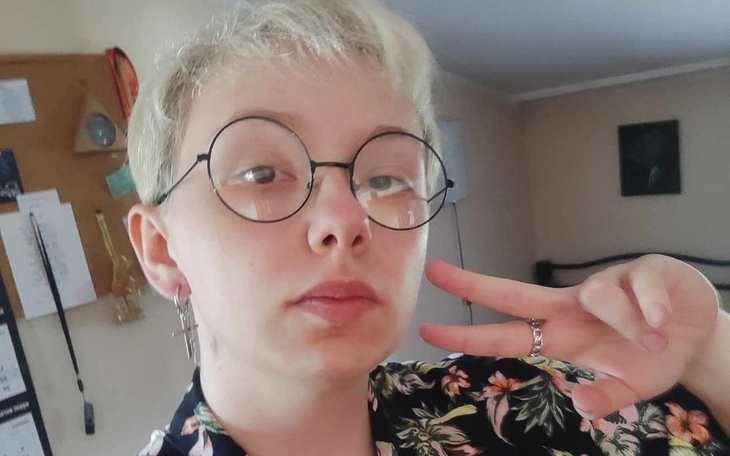 Młoda osoba w okularach, robiąca znak pokoju.