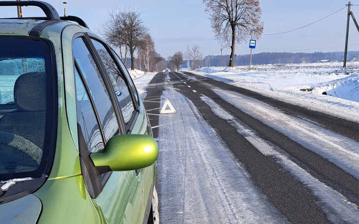Zielony samochód na zaśnieżonej drodze, z trójkątem ostrzegawczym.