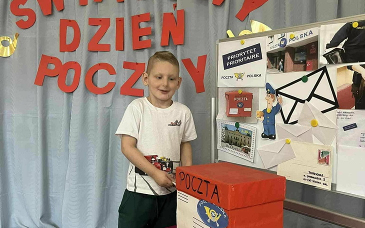Chłopiec przy skrzynce pocztowej, z uśmiechem na twarzy.