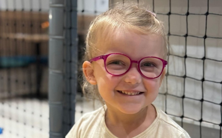 Uśmiechnięta dziewczynka w okularach, bawiąca się w przestrzeni rekreacyjnej.