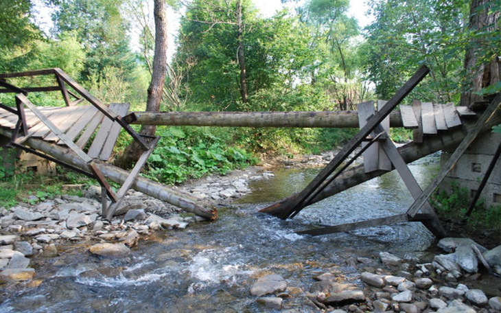 Zniszczony most nad strumieniem w lesie.