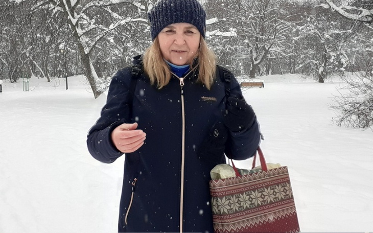 Kobieta w zimowej kurtce, trzymająca torbę, na tle zaśnieżonego parku.