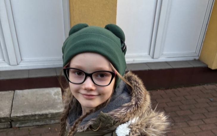 Dziewczynka w zielonej czapce i okularach, uśmiechająca się.