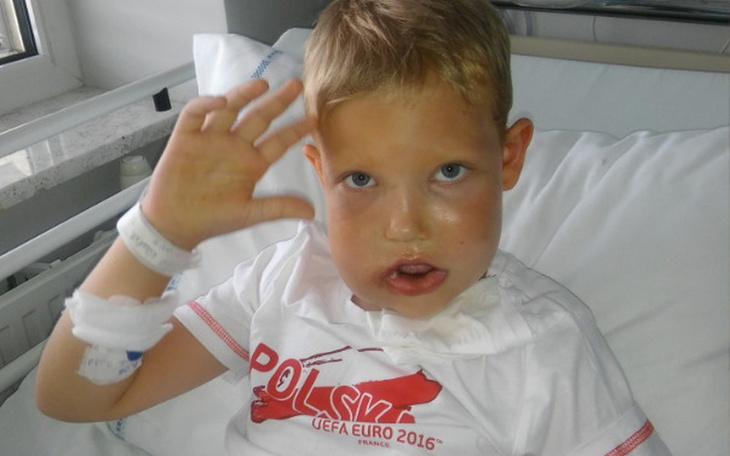 Chłopiec w szpitalu, machający ręką z uśmiechem.