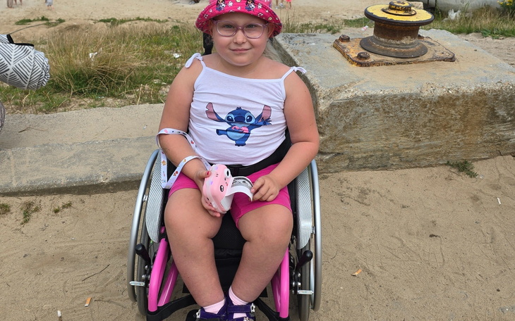 Dziewczynka w wózku inwalidzkim, uśmiechająca się na plaży.