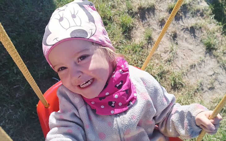 Uśmiechnięta dziewczynka na huśtawce w kolorowej chustce.