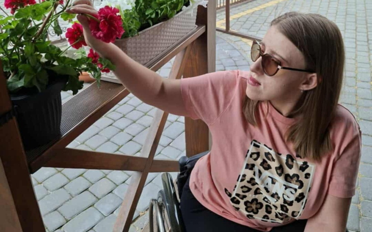 Kobieta w okularach przeciwsłonecznych, dotykająca kwiatów na tarasie.