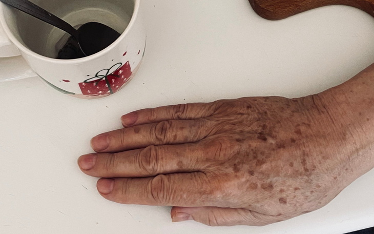 Dłoń starszej osoby na stole obok filiżanki.