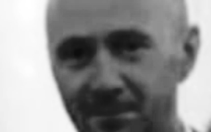 Człowiek w czarno-białym ujęciu, z tajemniczym wyrazem twarzy.