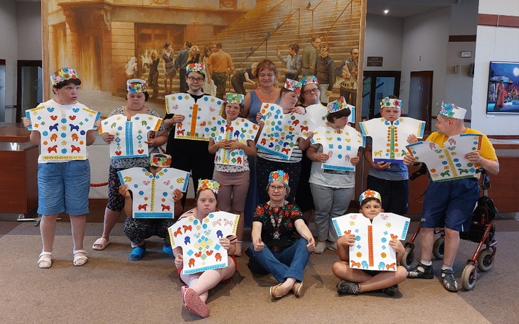 Grupa dzieci z kolorowymi kapeluszami i pracami plastycznymi.