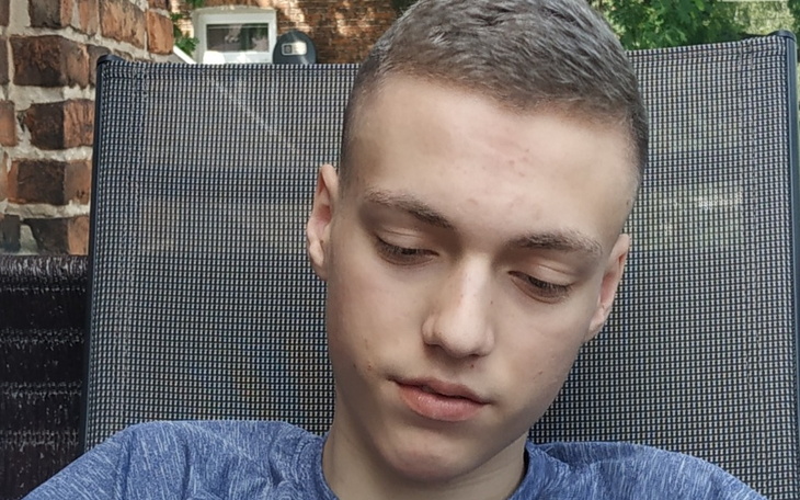 Młody chłopak w niebieskiej koszulce, skupiony na swoim telefonie.