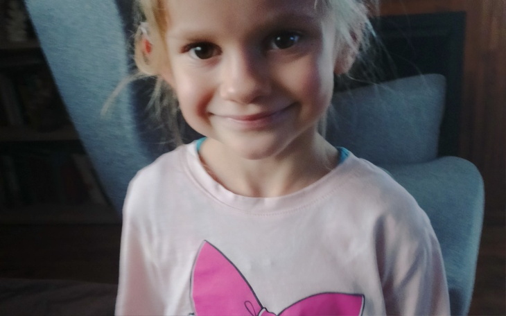 Uśmiechnięta dziewczynka w różowej koszulce z dużą kokardą.