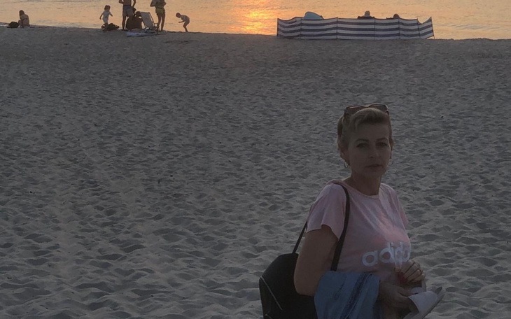 Kobieta w różowej koszulce na plaży, z zachodem słońca w tle.