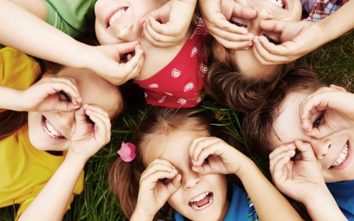 Grupa dzieci leżących na trawie, uśmiechających się.