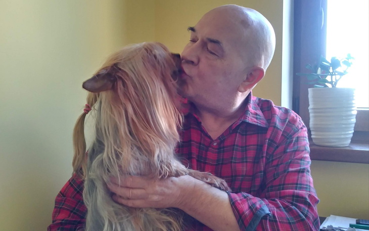 Mężczyzna całujący psa, obaj uśmiechnięci.