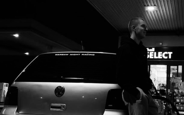 Mężczyzna oparty o samochód, w nocy, z logo na tylnej szybie.