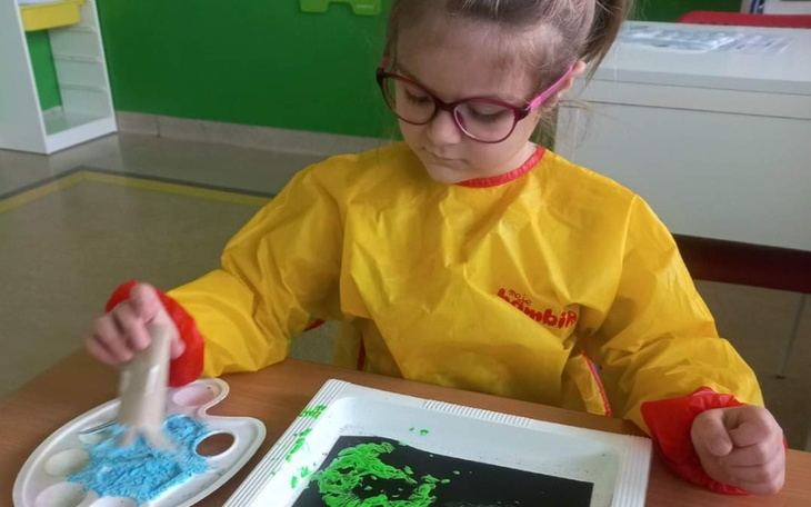 Dziewczynka w okularach maluje na czarnym papierze.