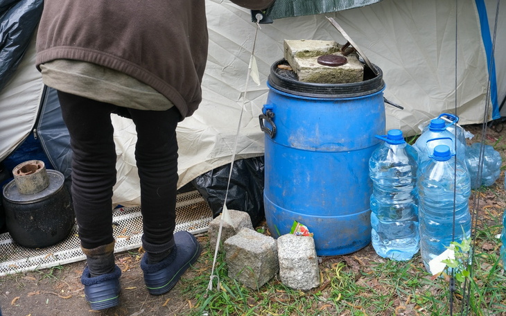 Osoba przy namiocie, zbierająca wodę i jedzenie.