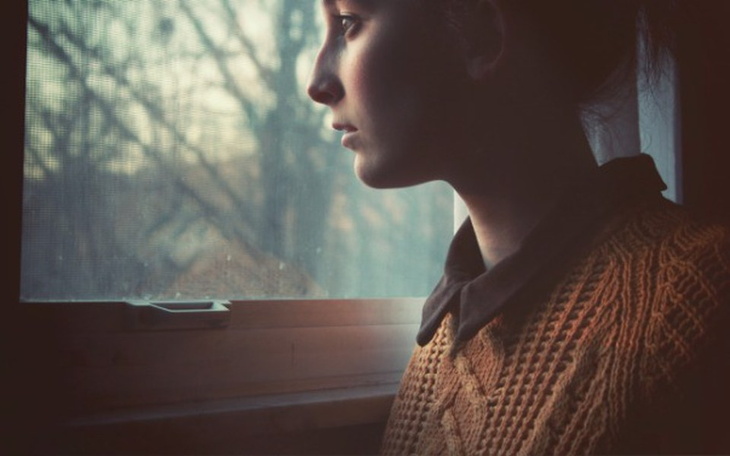 Kobieta patrząca przez okno, zamyślona i refleksyjna.