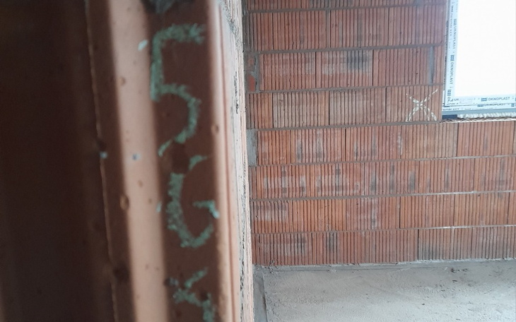 Fragment ściany z cegłami, z widocznymi numerami na tynku.