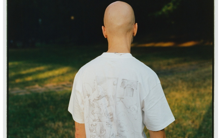 Osoba z tyłu w białej koszulce, na tle zielonej trawy.