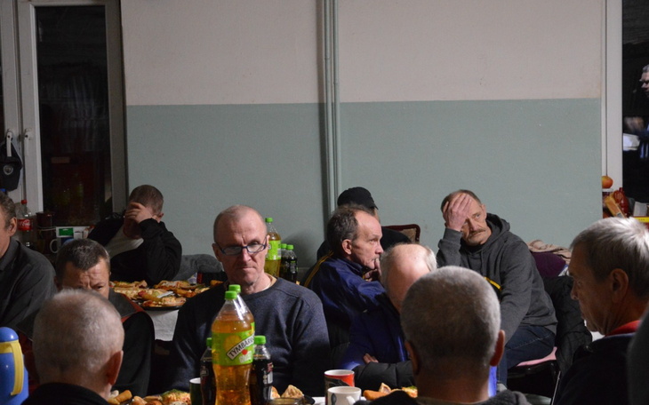 Grupa mężczyzn siedzących przy stole, jedzących posiłek.