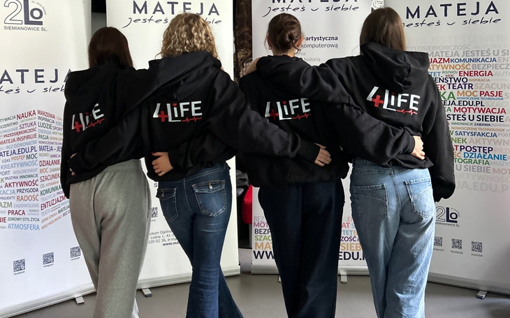 Cztery dziewczyny w bluzach, pozujące razem na tle banerów.