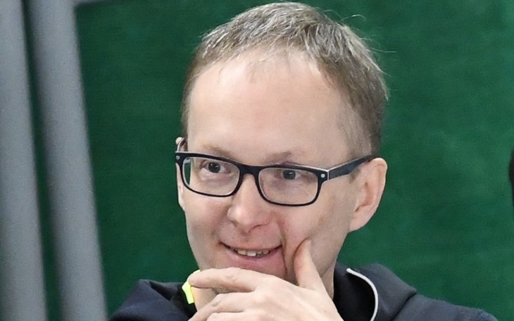 Mężczyzna z okularami uśmiechający się w trakcie rozmowy.