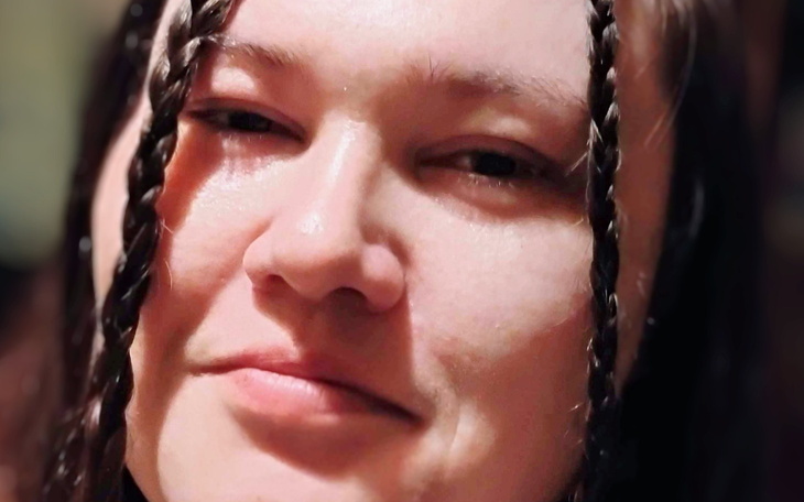 Kobieta z warkoczami, patrząca z uśmiechem w obiektyw.