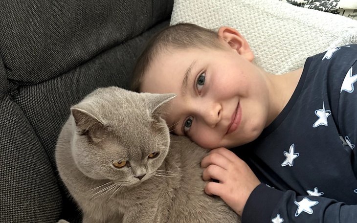 Chłopiec leży na kanapie z szarym kotem, obaj wyglądają na zrelaksowanych.