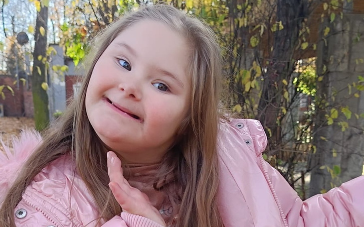 Dziewczynka w różowej kurtce uśmiecha się na tle jesiennych liści.