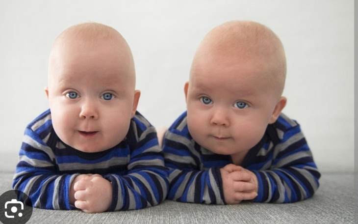 Dwa niemowlęta leżące obok siebie, urocze i uśmiechnięte.