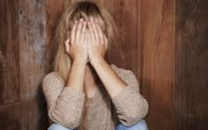 Kobieta z zasłoniętą twarzą siedzi na podłodze.