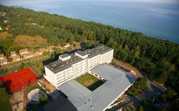 Widok na hotel nad morzem, otoczony lasem i zielenią.