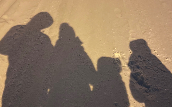 Cienie czterech osób na zaśnieżonej drodze.