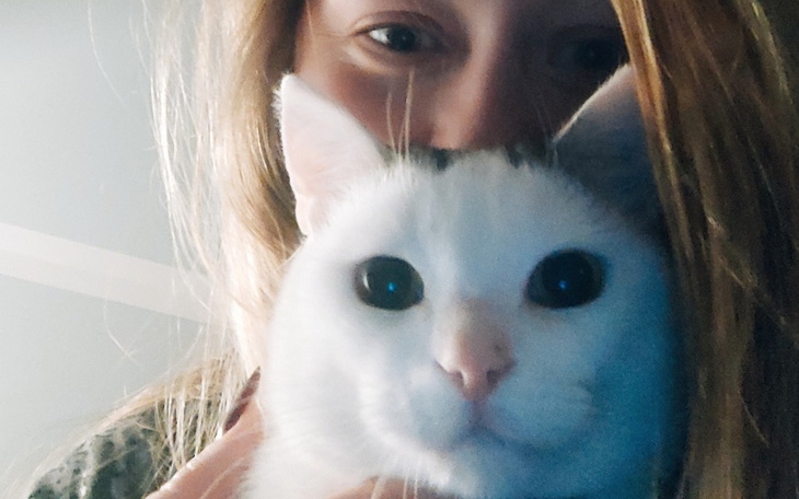 Dziewczyna trzymająca białego kota blisko twarzy.