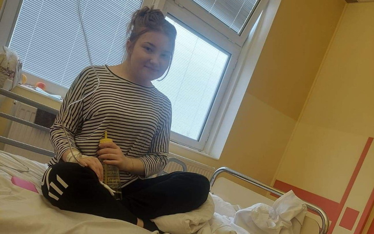 Młoda dziewczyna siedzi na łóżku w szpitalu, trzymając butelkę.