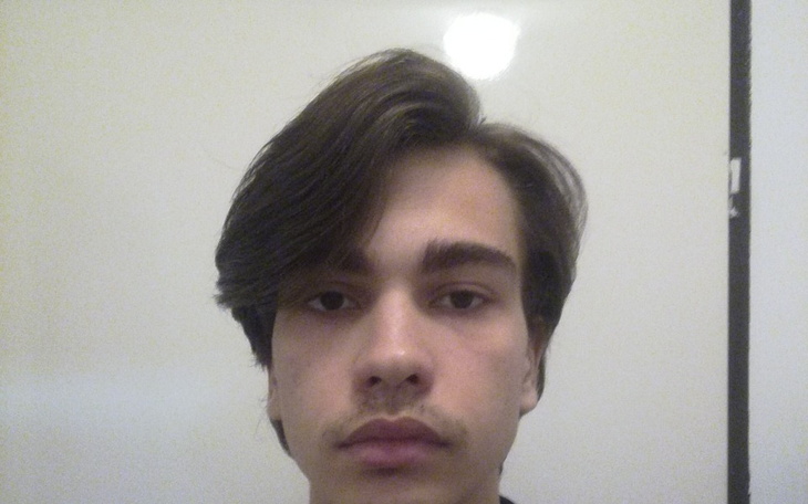 Młody mężczyzna patrzący w kamerę, z długimi włosami.