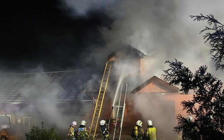 Pożar budynku z interweniującymi strażakami.