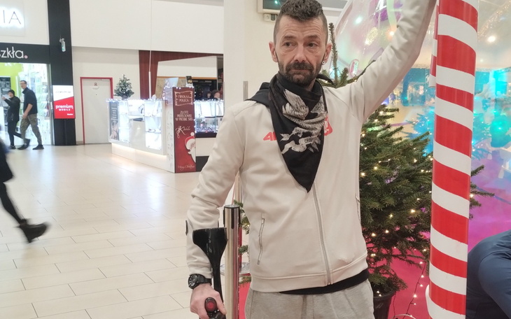 Mężczyzna w sklepie, trzymający laskę, z dekoracjami świątecznymi w tle.