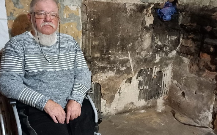 Starszy mężczyzna w wózku inwalidzkim, w zniszczonym pomieszczeniu.
