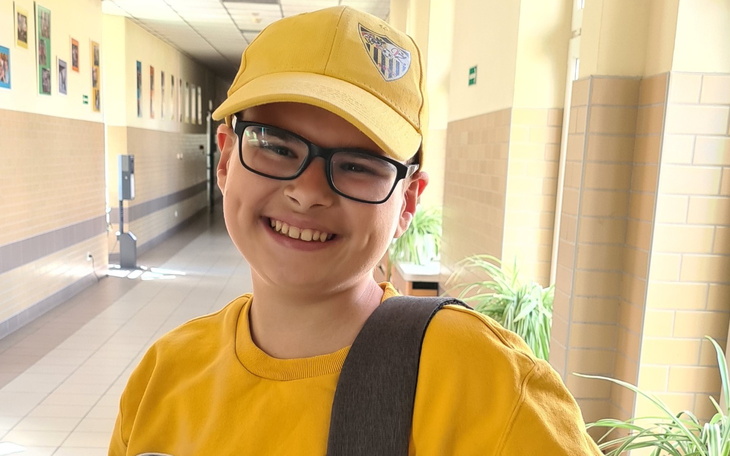 Uśmiechnięty chłopiec w żółtej czapce i koszulce, stojący w korytarzu.