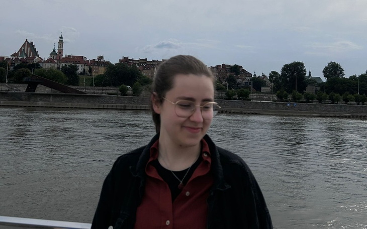 Osoba na tle rzeki i miasta, uśmiechnięta.